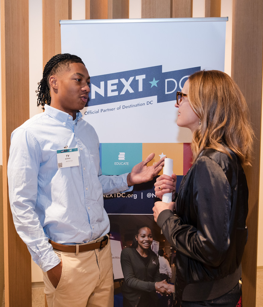 A young Black man networks with a White woman with the NEXTDC banner in the background