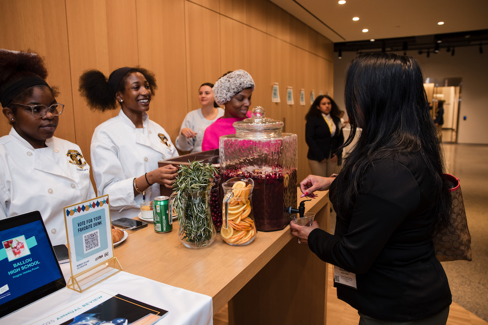 Two young Black female culinary arts students host the drink station at the Destination DC holiday celebration