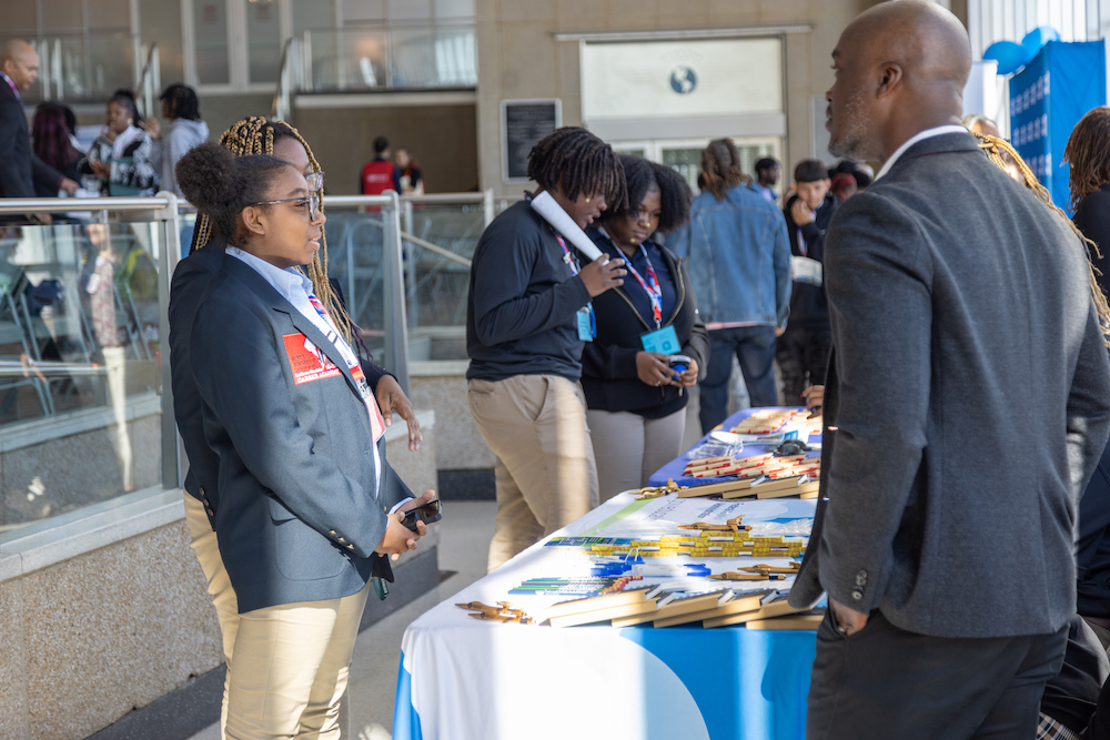 Two young Black ladies chat with a representative from American Airlines during the MWAA Career Expo